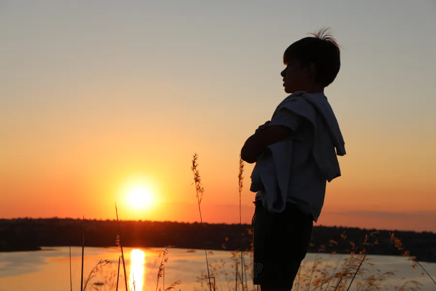 Silhouette d'un enfant face au coucher du soleil au bord de l'eau